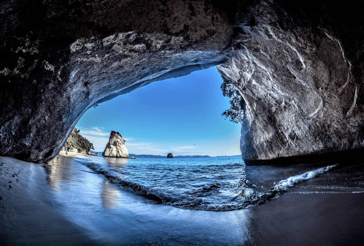 View from inside a grotto on the beach, with waves and rocks in the background, creating a peaceful atmosphere.