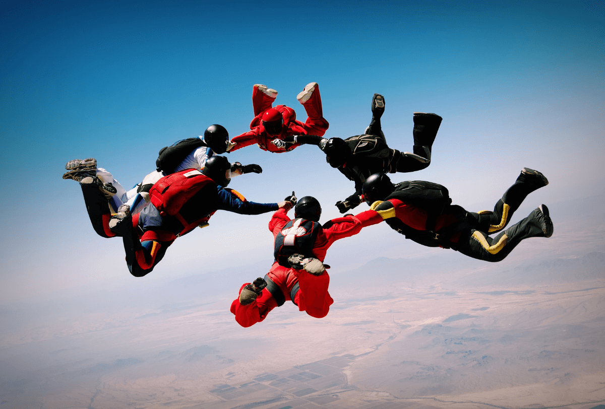 Paratroopers jump from a plane, floating in the blue sky, ready to deploy their parachutes.