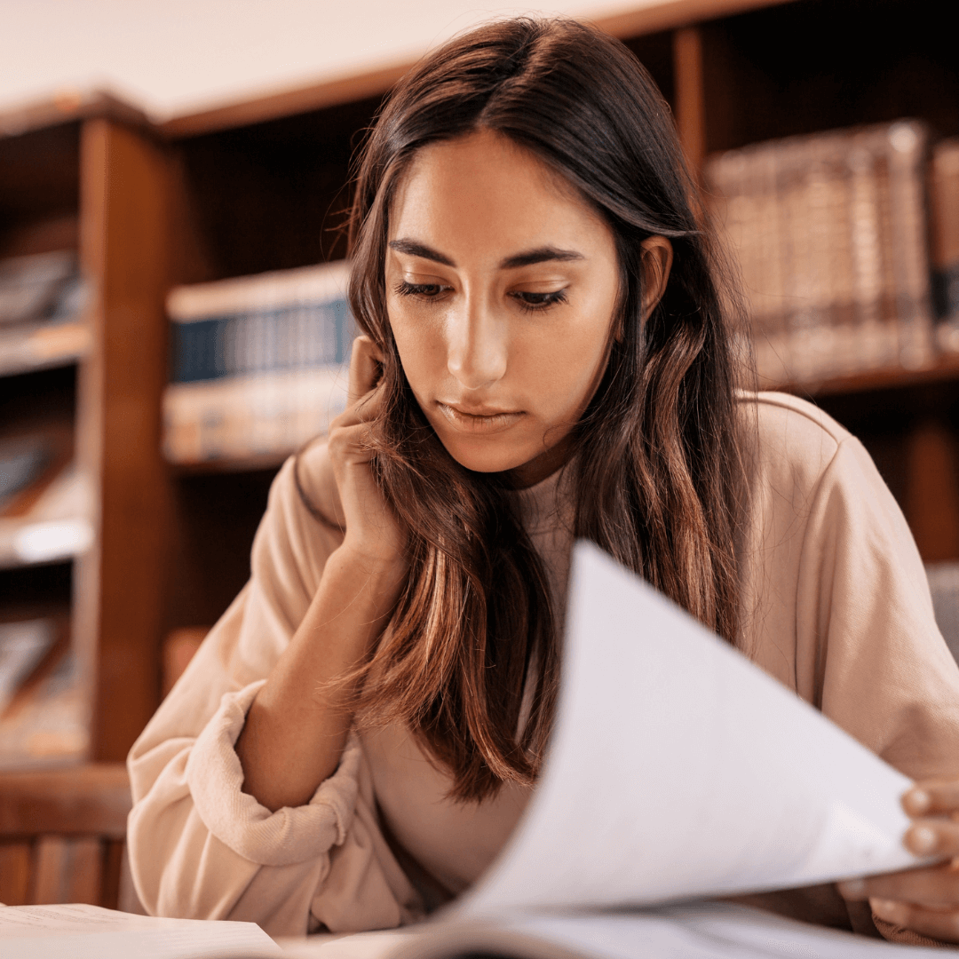 Une femme lit un journal dans une bibliothèque, entourée de livres et d'un environnement calme et studieux.