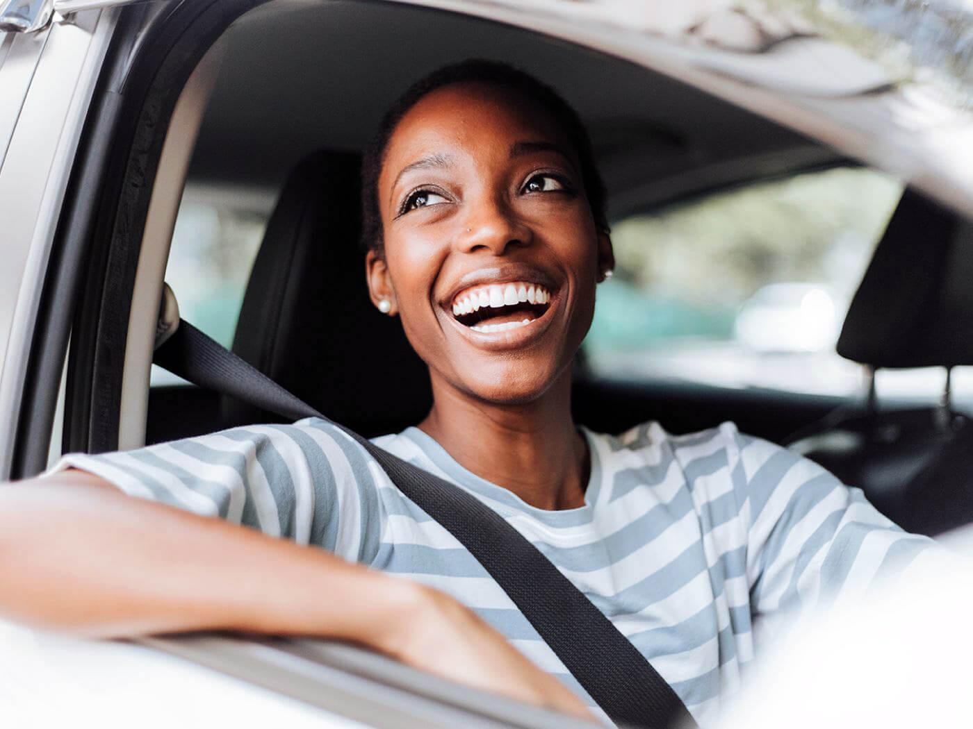 Une femme souriante assise dans une voiture, affichant une expression joyeuse et accueillante.