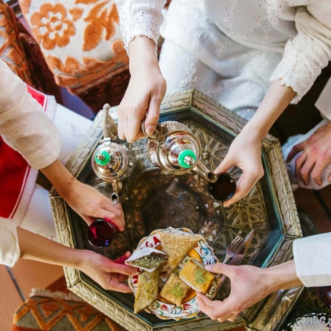 A group of people gathering around cups of tea and tasty dishes, sharing a convivial moment.