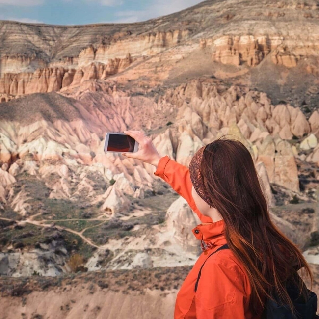 A woman taking a photo of the landscape with her phone, capturing the beauty of the surrounding nature.