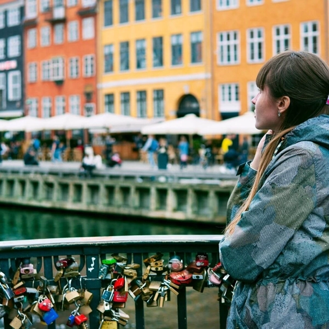 A woman contemplating a bridge adorned with padlocks, a symbol of love and commitment, under a clear sky.