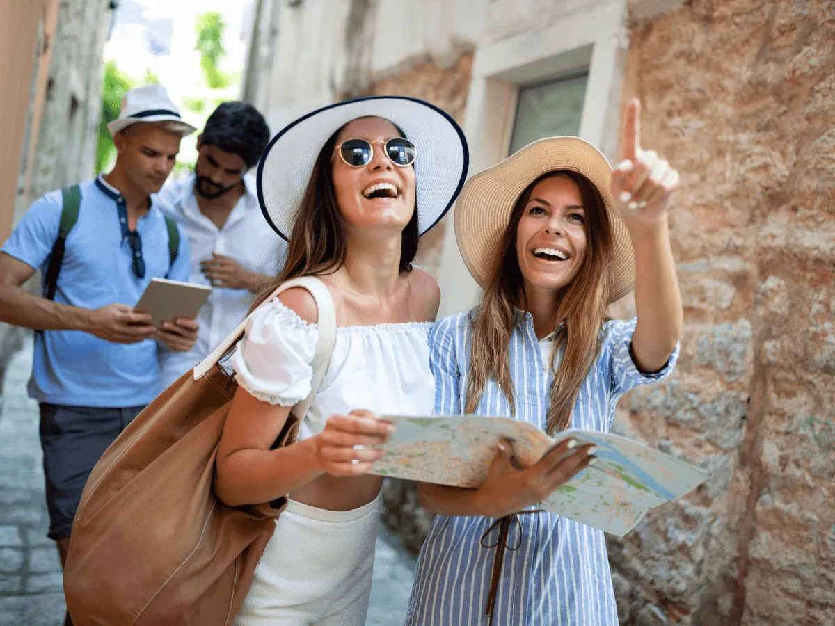 Deux femmes portant des chapeaux et des lunettes de soleil marchent dans une rue ensoleillée.