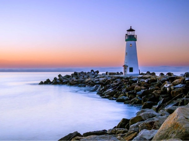 Un phare se dresse sur les rochers, illuminé par la lumière dorée du coucher de soleil.