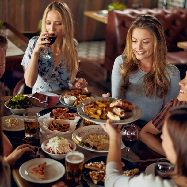 Un groupe de femmes partageant un repas et dégustant du vin dans une ambiance conviviale et joyeuse.