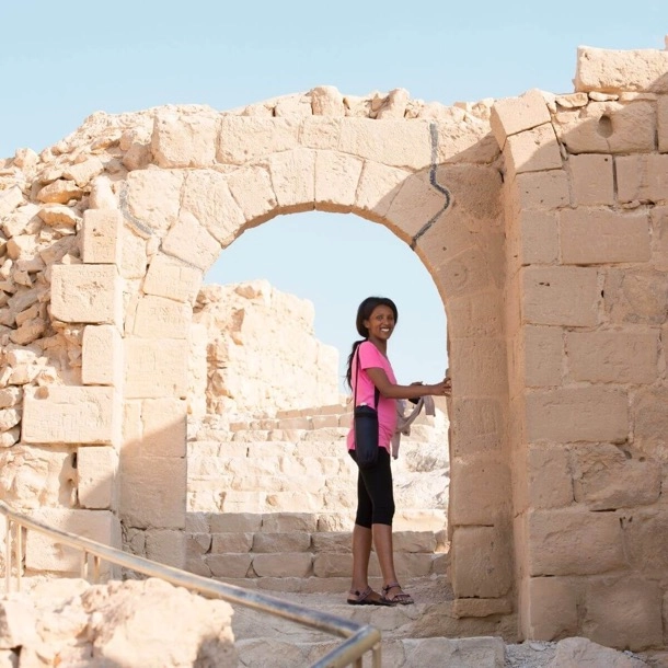 Une femme se tenant dans une arche d'un bâtiment en pierre, entourée d'une architecture historique et élégante.