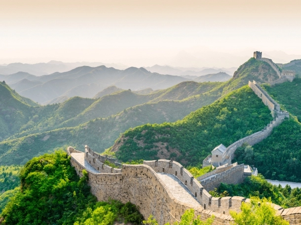 Vue aérienne de la Grande Muraille de Chine, serpentant à travers les montagnes verdoyantes et le paysage environnant.