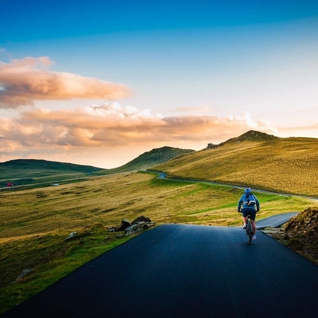 A person pedals along a picturesque road through the countryside, surrounded by greenery and natural landscapes.