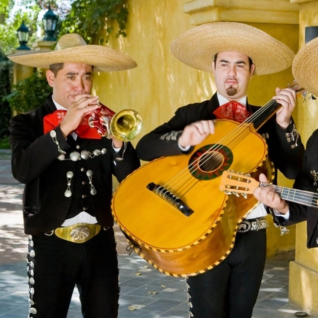 Trois hommes en costumes mexicains jouent des instruments de musique, créant une ambiance festive et colorée.