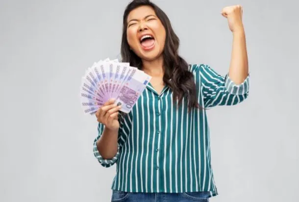 Une femme avec une liasse de billets en éventail dans sa main droite qui fait un signe de victoire avec sa main gauche
