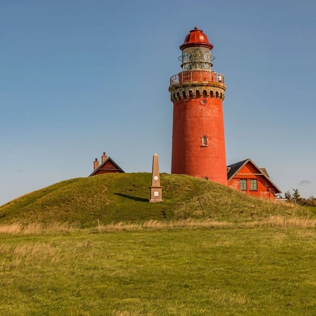 A red lighthouse perched on a hill, standing majestically against the blue sky.