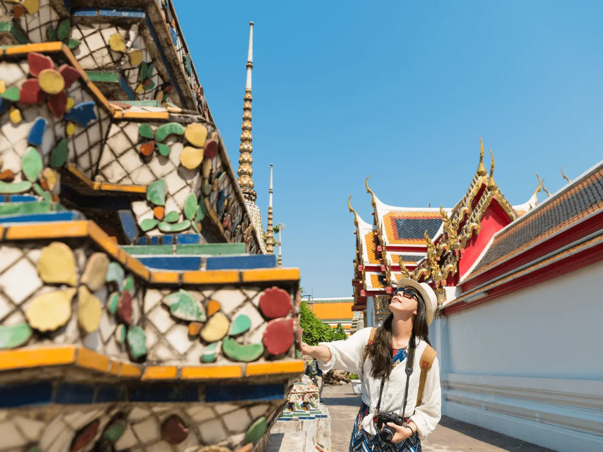 Une femme portant un chapeau et des lunettes de soleil admire l'architecture d'un temple majestueux.