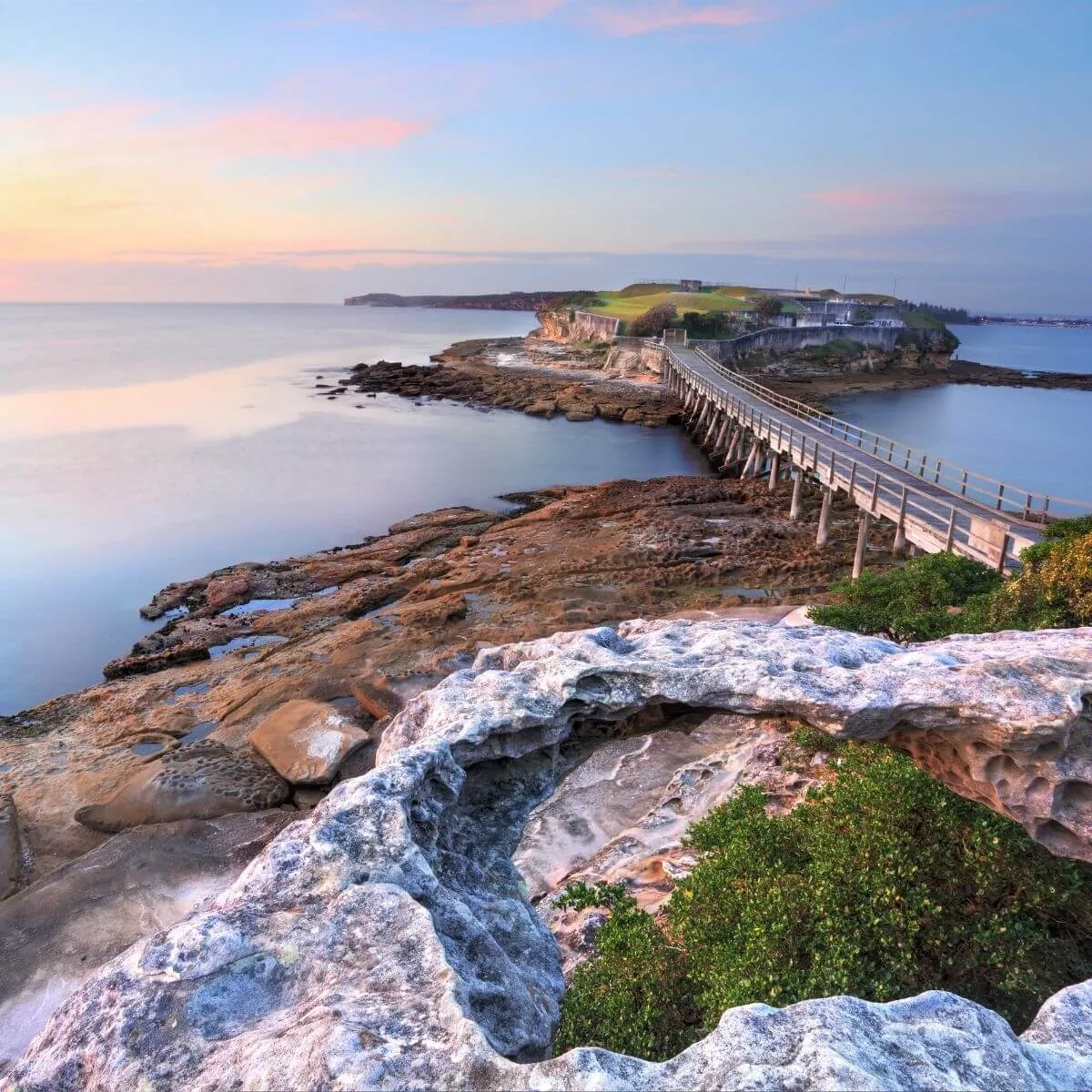 Sunset over the ocean, illuminating the rocky coastline in a soothing golden light.