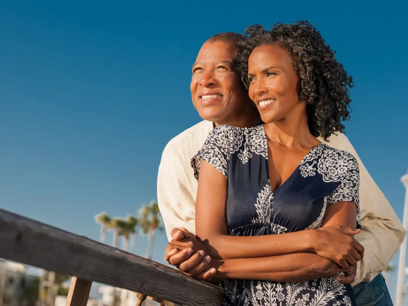 A couple stands together on a dock, under a clear blue sky, enjoying a serene moment by the water.