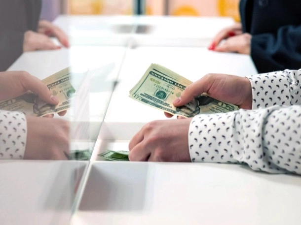 A person counts cash at a counter, focusing intently on the money in their hands.