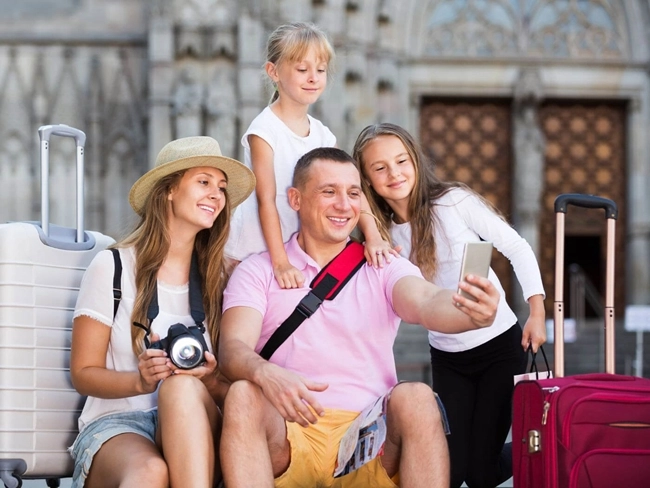 Une famille pose pour un selfie avec des bagages et un appareil photo, capturant un moment de joie ensemble au cours de leurs voyages.