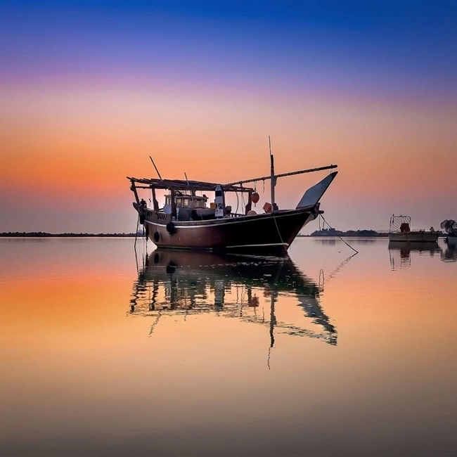 Un bateau amarré au coucher du soleil, reflétant des couleurs chaudes sur l'eau calme.