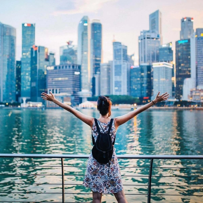 Femme debout sur un pont, les bras écartés, devant la silhouette d'une ville moderne.