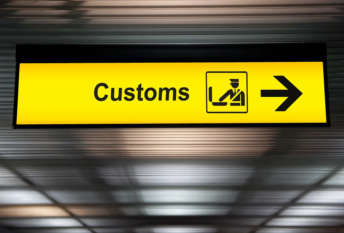 Un panneau portant l'inscription « Customs » (douanes) est placé au-dessus d'une flèche jaune vif qui dirige les voyageurs.