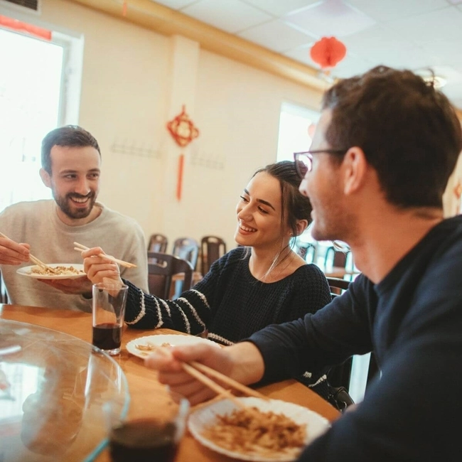 Three people enjoy a meal together at a restaurant table, sharing a convivial and pleasant moment.