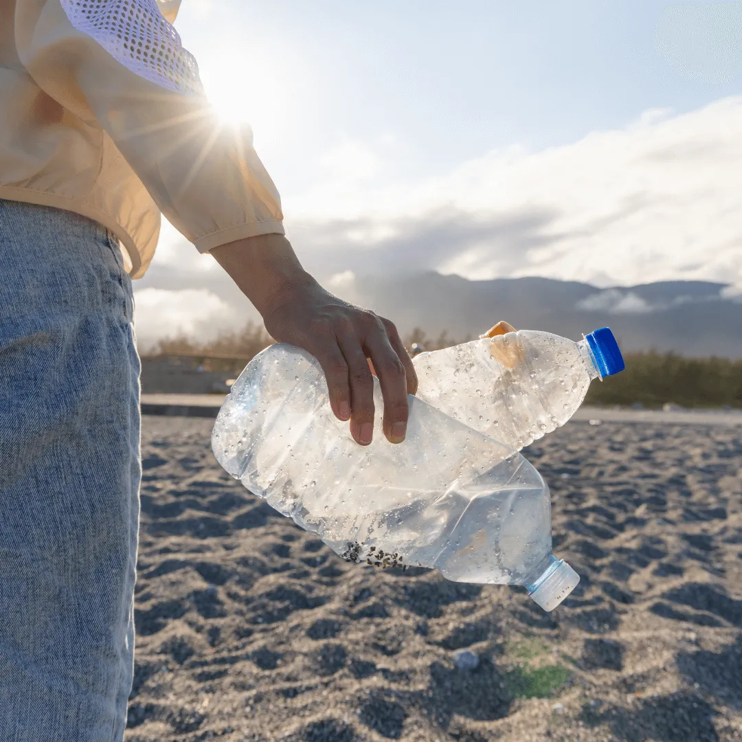 Une personne tenant deux bouteilles en plastique sur la plage, soulignant l'impact de la pollution marine.