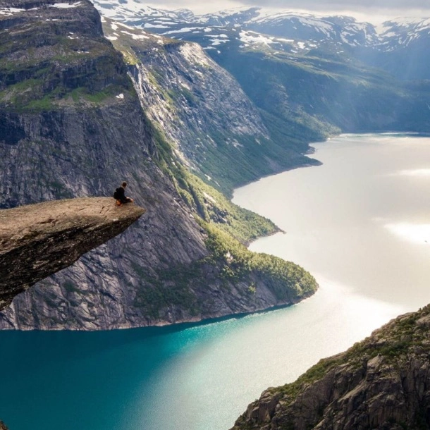 Une personne assise au sommet d'une falaise, contemplant un lac paisible en contrebas.