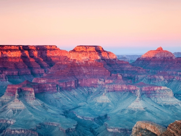 Vue du Grand Canyon au coucher du soleil, illuminant les roches avec des teintes orange et violettes spectaculaires.