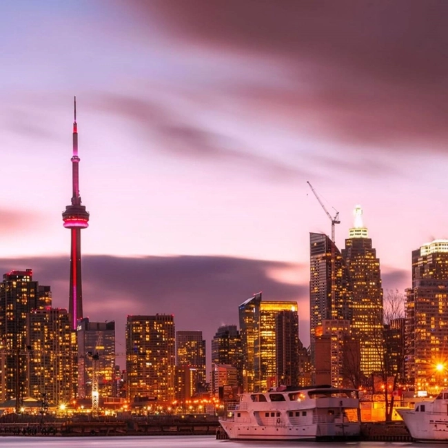  Vue du skyline de Toronto au crépuscule, illuminé par les lumières des bâtiments et le reflet sur l'eau.