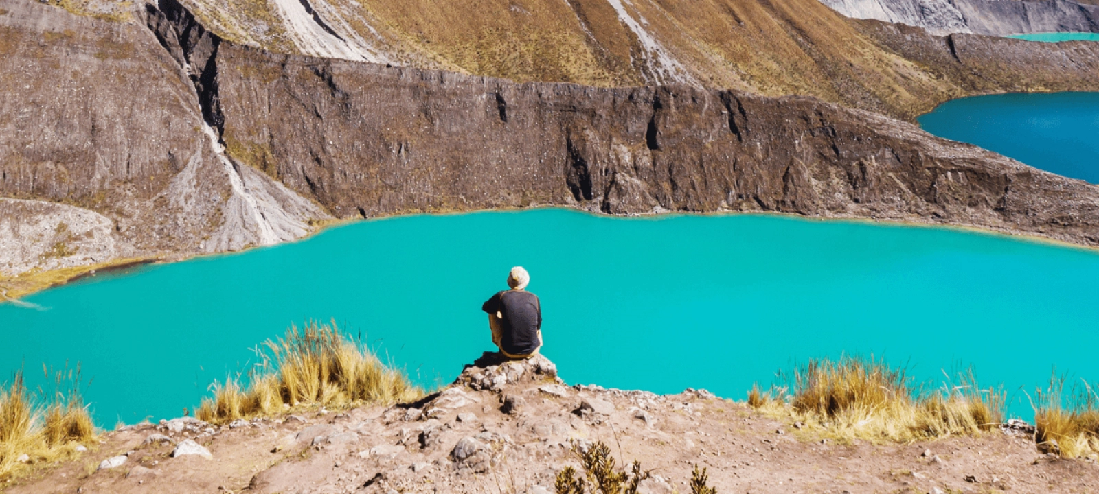 Un homme se tient sur un rocher, contemplant un lac turquoise scintillant sous le soleil.