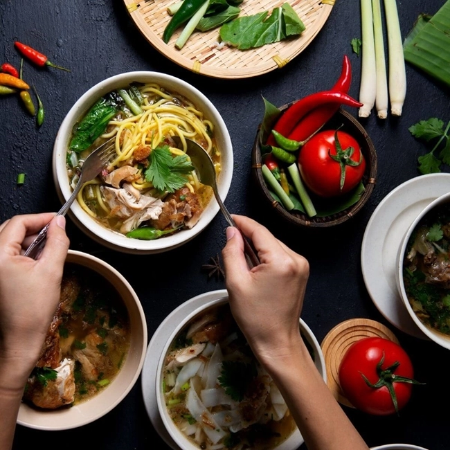 Hands holding bowls of food containing vegetables and meat, illustrating a tasty, balanced meal.