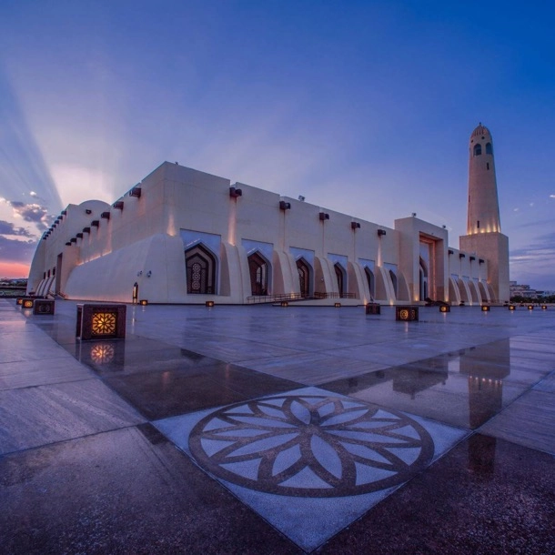 Mosquée au coucher du soleil, illuminée par des teintes dorées, au cœur d'une ville animée.