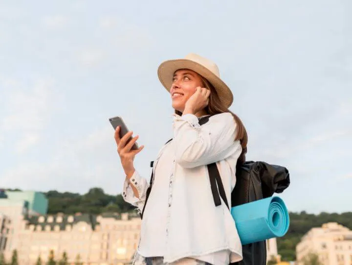 A woman wearing a hat and a white shirt is engaged in a conversation on her cell phone.