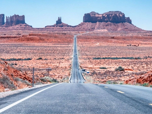 Route menant à Monument Valley, avec des formations rocheuses emblématiques sous un ciel bleu dégagé.