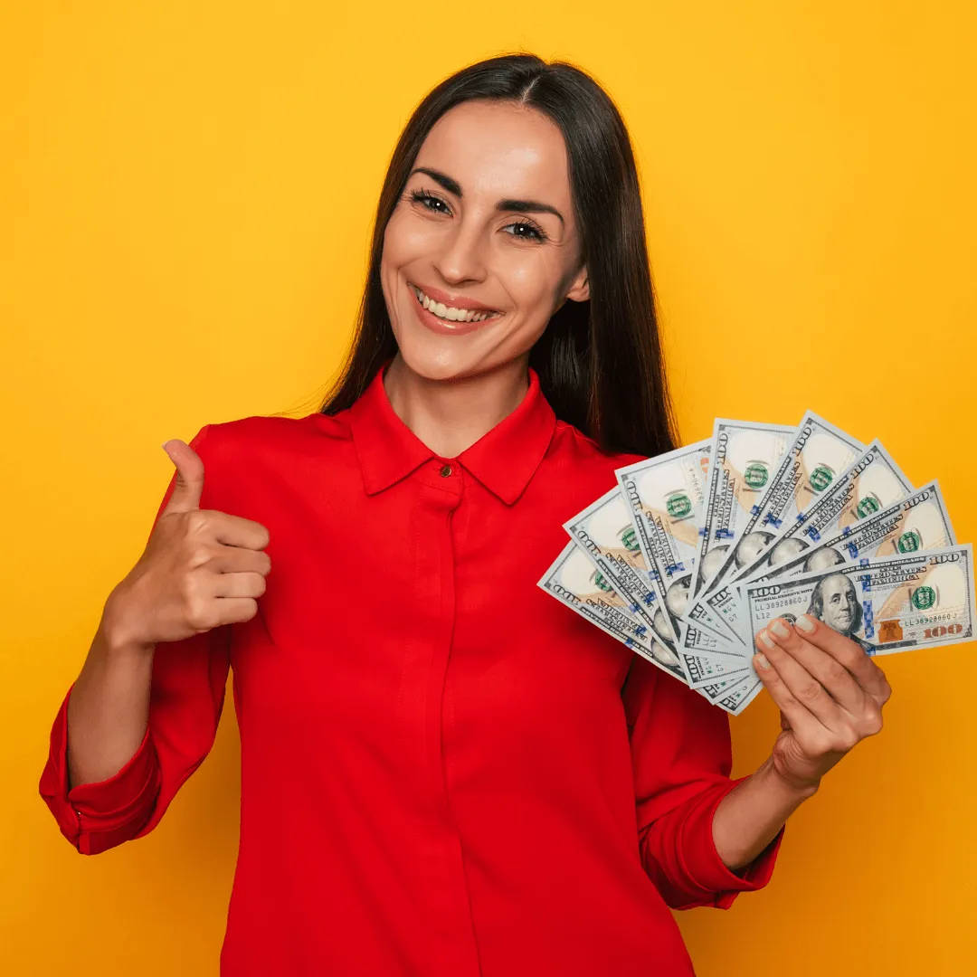 Une femme souriante tenant une liasse de billets tout en faisant un signe de pouce levé, exprimant sa satisfaction.