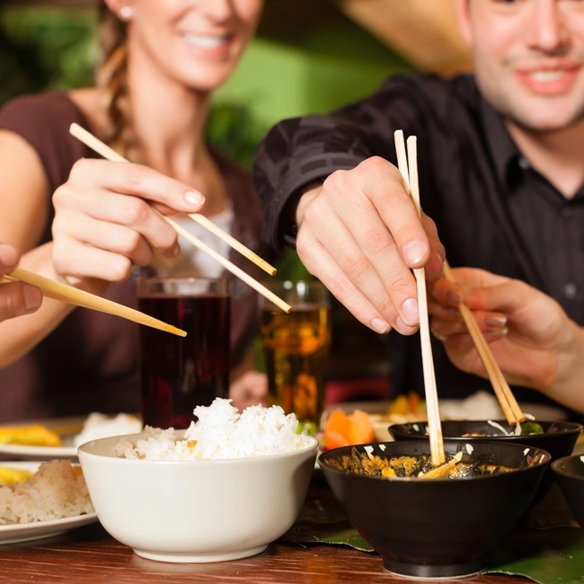 A group of people enjoying food in a restaurant, using chopsticks to eat.