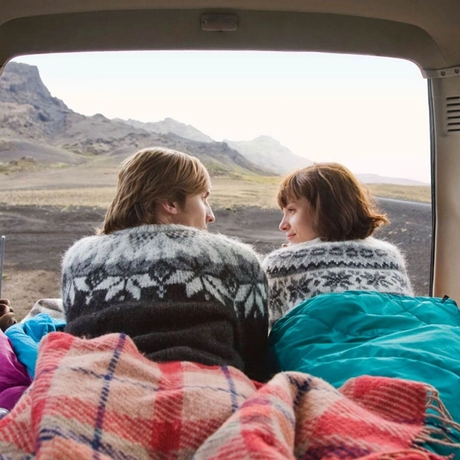 Two people sitting in the back of a car, wrapped in blankets, enjoying a moment of relaxation.