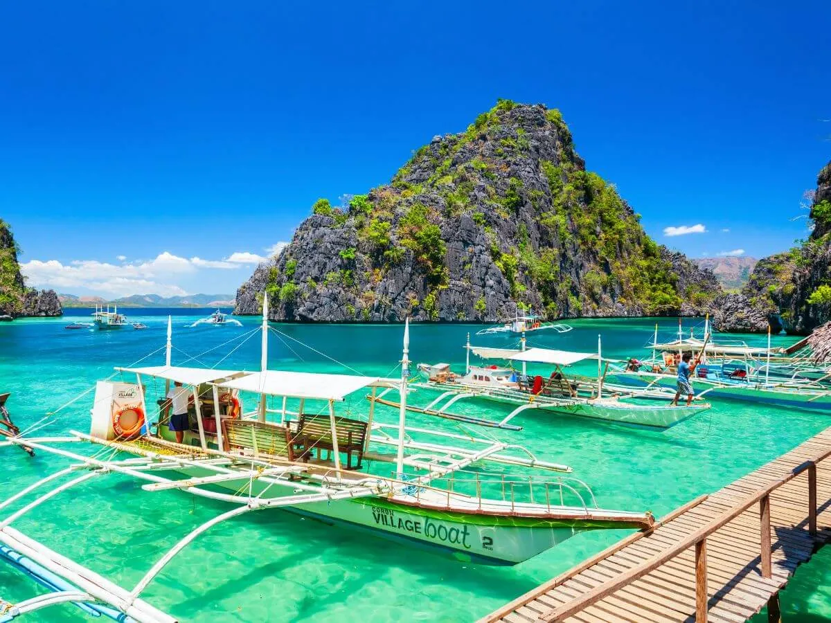 Boats moored in the crystal-clear waters of a tropical island, surrounded by lush landscapes and sunny skies.