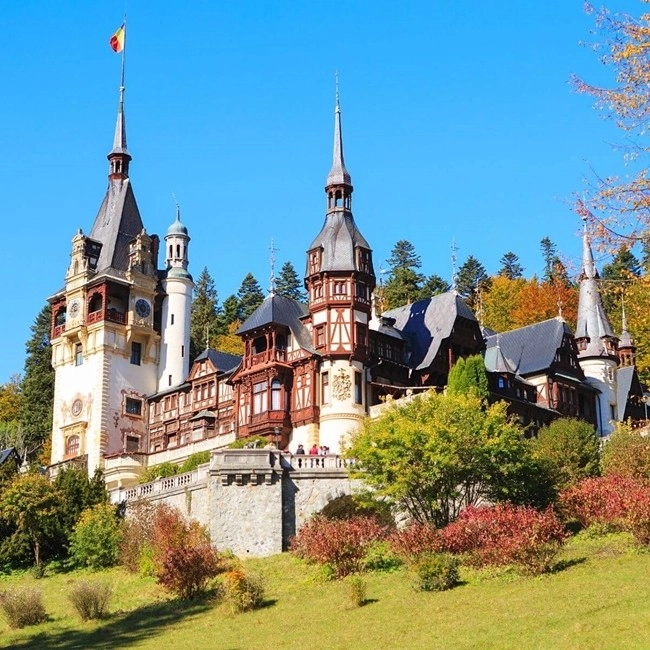 A majestic chateau surrounded by trees, adorned with numerous turrets, stands in a verdant landscape.