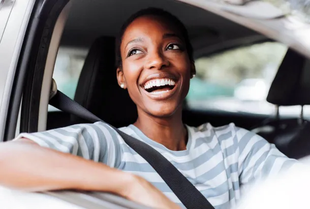 Une femme souriante assise dans une voiture, affichant une expression joyeuse et accueillante.