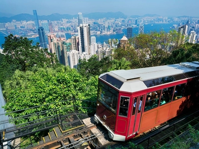 A red streetcar climbs a hill, with a picturesque city in the background, illustrating a dynamic urban landscape.