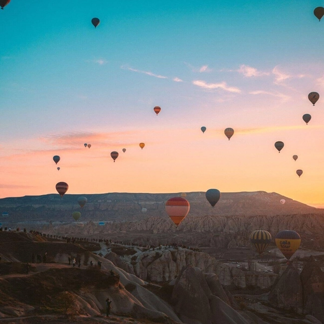  Many colorful hot-air balloons soar over a majestic mountain range under clear skies.