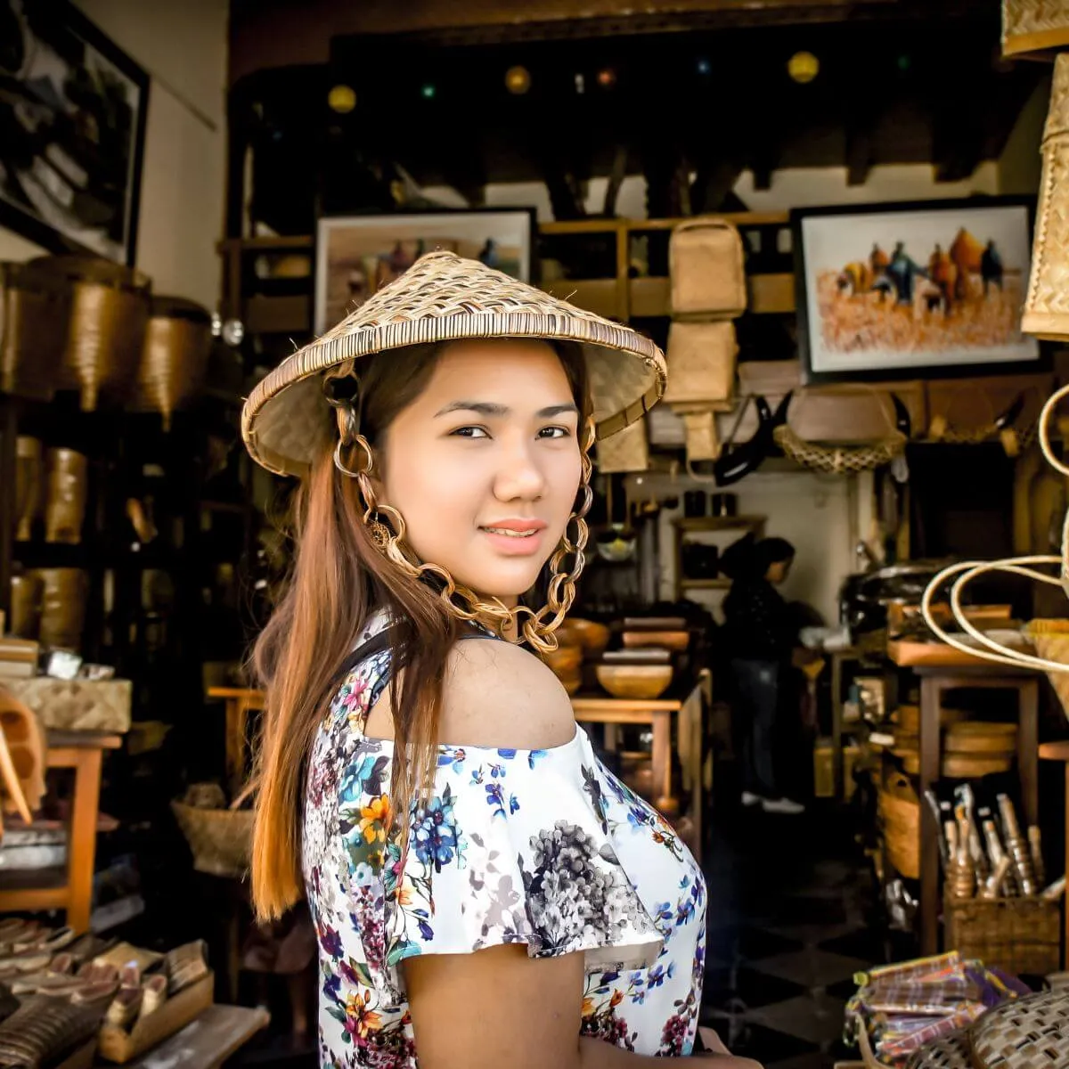 A woman wearing a hat stands in a store, surrounded by various items for sale.