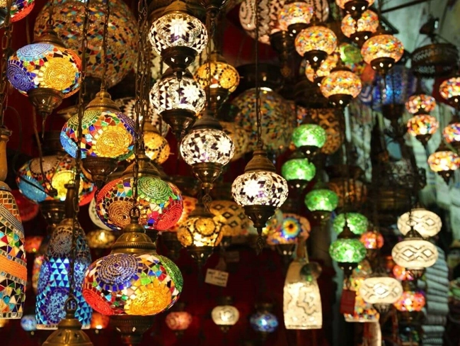  Many colorful lamps hanging from the ceiling of a store, creating a warm, welcoming atmosphere.