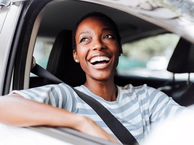 Une femme souriante est assise dans une voiture, rayonnant de joie et de positivité alors qu'elle profite de son trajet.