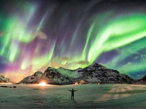 Une personne se tenant dans la neige sous une aurore boréale verte et violette illuminant le ciel nocturne.