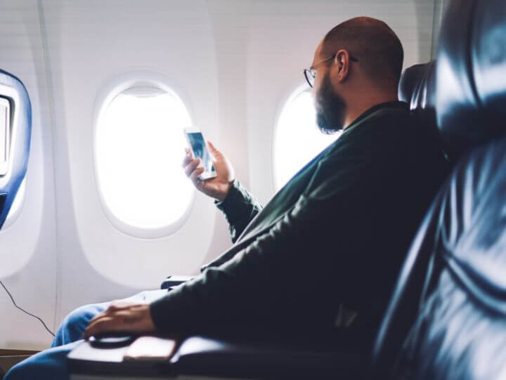 A man holding a phone in his hand sitting in an airplane and looking at a window