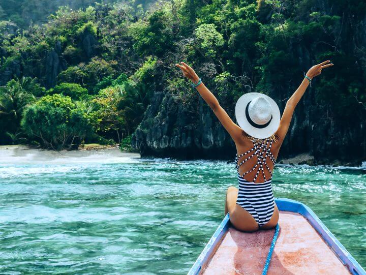 Woman in striped swimsuit and hat sitting on boat in the ocean, enjoying a sunny day at sea.